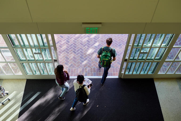 Three students walking through an automatic door as they exit a building